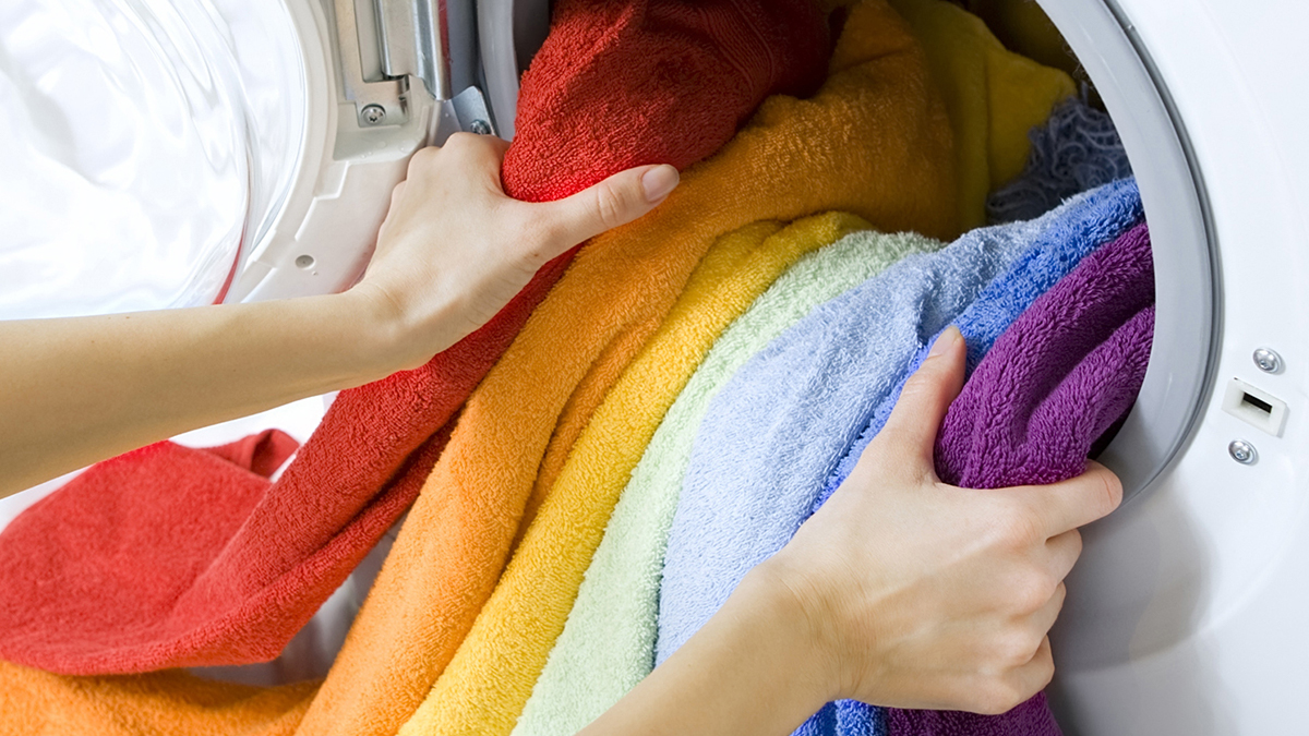 rainbow clothing being loaded into front loader washing machine