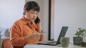person on phone to bank while holding credit card and looking at laptop