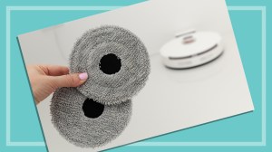 hand holding mopping pads with robot vacuum in background